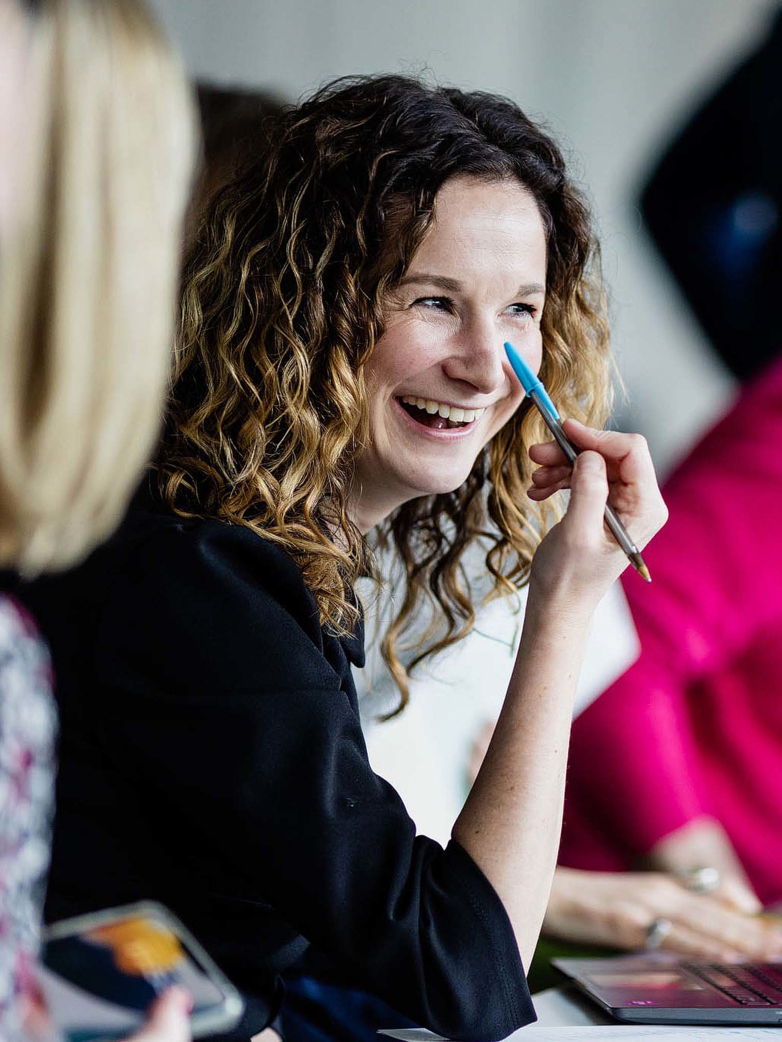 Lady laughing in a meeting holding a pen