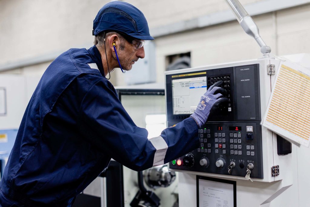 Man in blue work clothes and blue hard hat working a machine