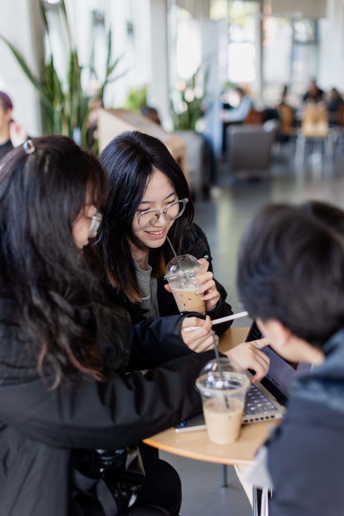 people smiling and drinking from a straw whilst looking at a laptop