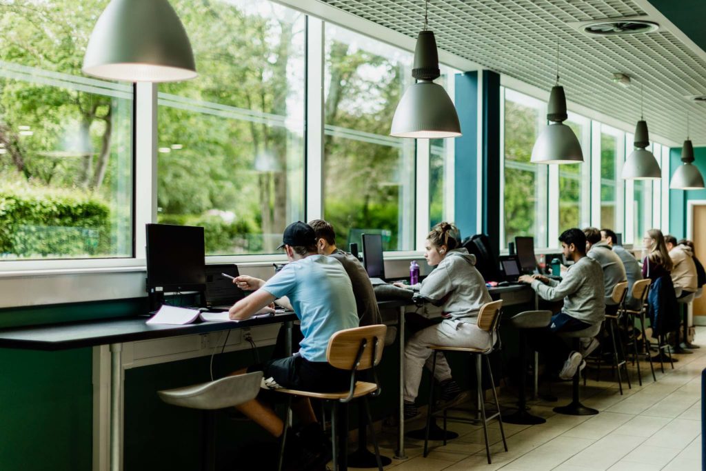 students sat down working on laptops indoors